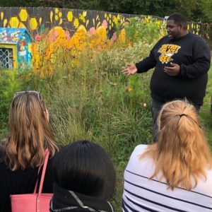 A man gesturing to a patch of wildflowers along a fence as onlookers watch