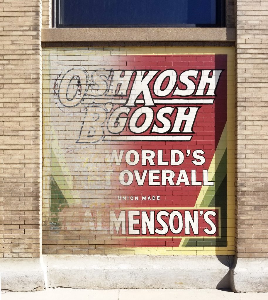 A before and after composite image showing an advertisement for OshKosh B'Gosh overalls that is faded and grey on the left but vibrant and recolorized on the right.