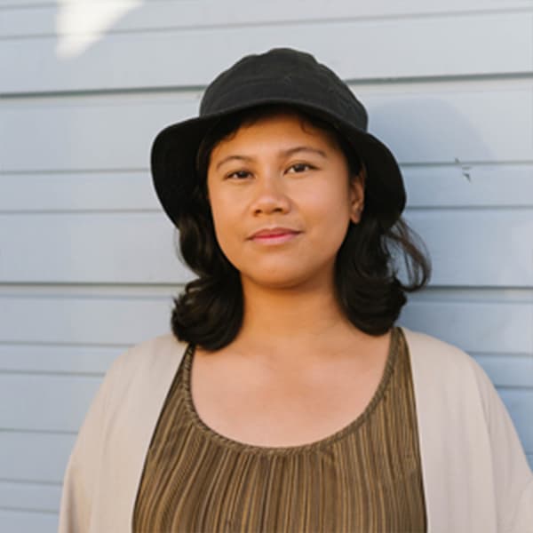 A woman with black hair and a black hat, standing outside smiling.