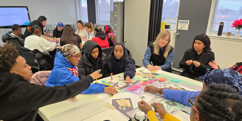Group seated around tables indoors, collaborating on a hands-on planning activity with craft materials and sticky notes.