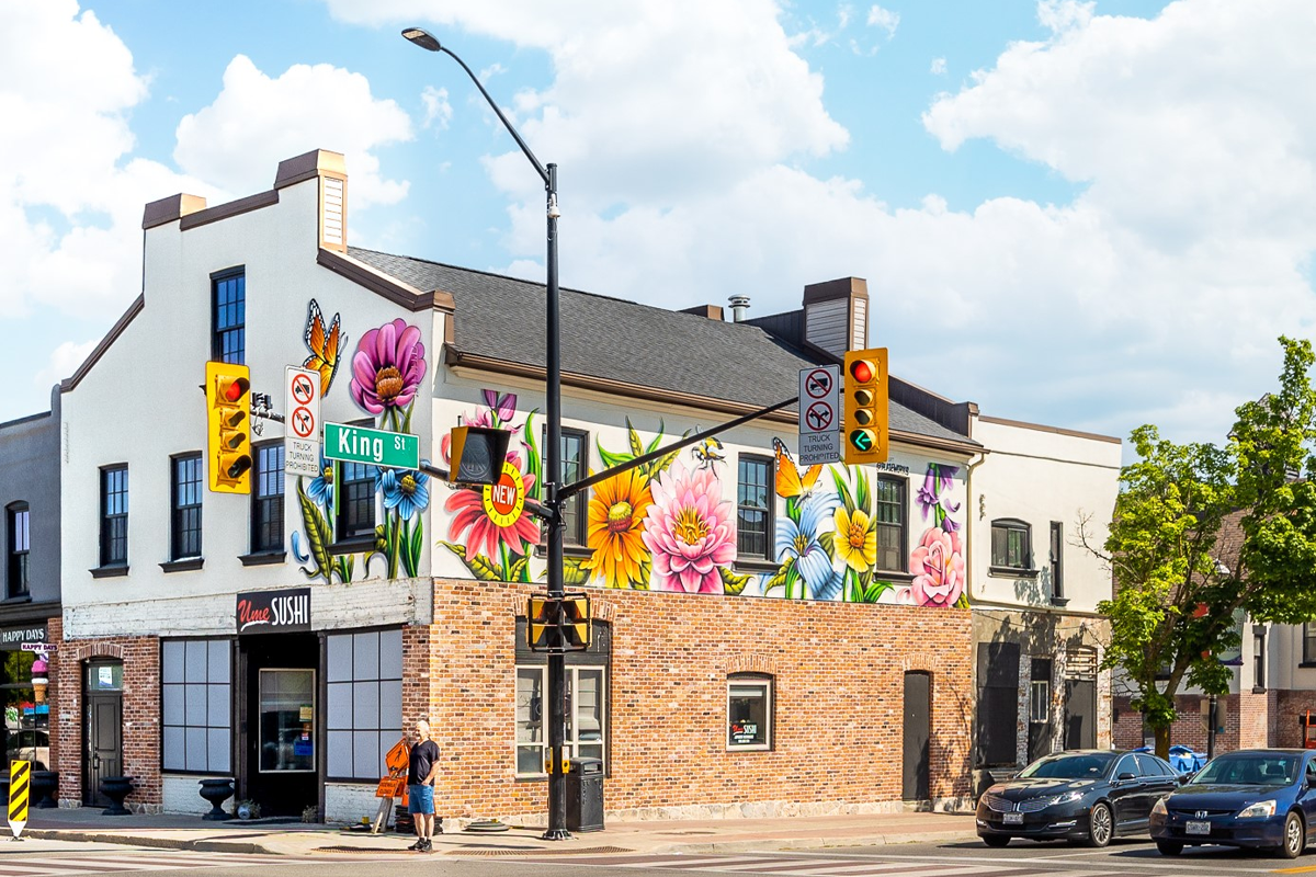 A corner building at King Street features a large, colorful floral mural covering the upper exterior walls. The mural shows oversized flowers and butterflies. Several cars wait at the traffic light in front of the building.